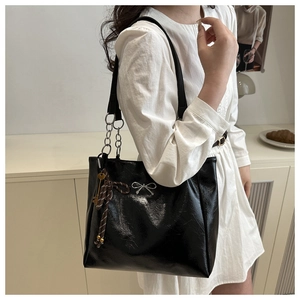 Detailed macro view of black glossy crinkled tote bag with silver bow accent and chain strap
