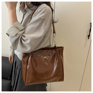 Detail of a brown glossy leather tote bag with a silver metal bow buckle and chain strap