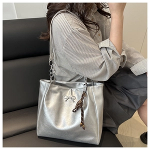Detail of silver tote bag featuring metal bow ornament and woven drawstring charm