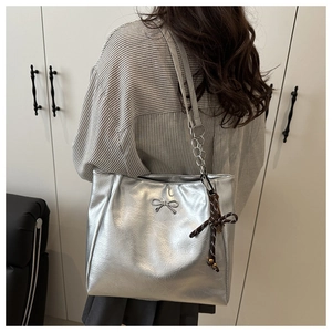 Detail of silver metallic tote bag featuring a bow charm and pleated leather texture