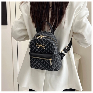 Rear view of a model wearing a mini black patterned backpack with gold hardware