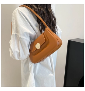 Dettaglio borsa sottobraccio marrone caramello con fibbia a cuore dorata su camicia bianca