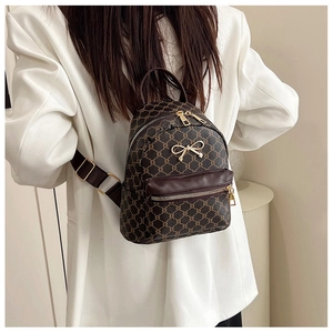 Detailed view of mini backpack featuring retro monogram print and golden metal bow charm