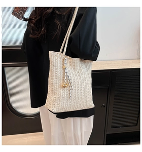 Detail view of cream woven straw tote bag with textured stripes and gold bell charm