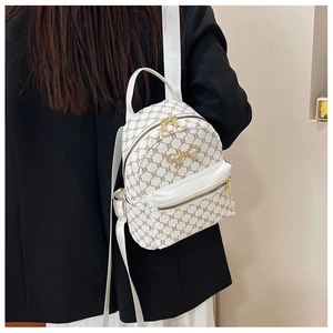 Detail of white mini backpack with geometric pattern and gold bow worn on black blazer