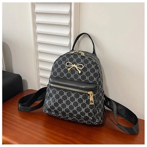 Detail of mini black backpack with gold bow hardware and chain pattern on wood surface