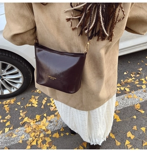 Detail of dark brown glossy leather crossbody bag with gold fashion lettering and hardware