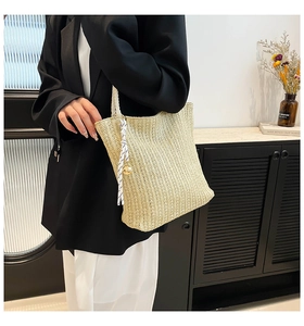 Detail of straw woven tote bag with white rope handles and decorative charms on a model