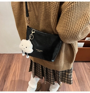 Glossy black bucket bag with gold hardware and white cloud plush charm on a model
