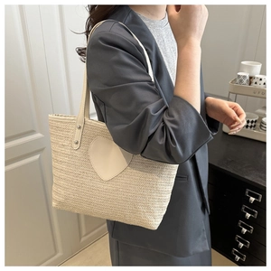 Detail of a straw bucket bag with white heart patch worn by a model in casual grey suit