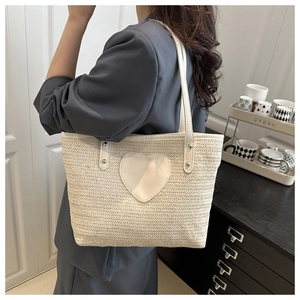 Detail of cream woven tote bag with leather heart patch and silver rivets on shoulder straps