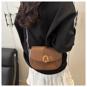 Brown leather saddle bag with gold U-shaped buckle shown on model in a modern setting