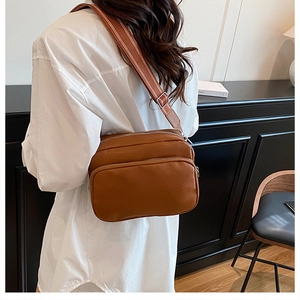 Detail of caramel crossbody bag with litchi texture, double zippers, and wide strap