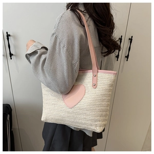 Detail of woven straw tote bag featuring a pink heart patch and matching leather strap
