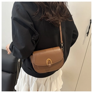 Detail view of brown saddle bag featuring a gold horseshoe clasp and sleek leather strap