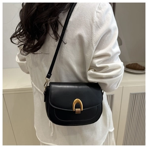 Detail of a minimalist black leather saddle bag with gold metal hardware on model