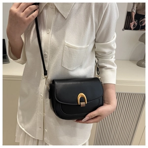 Detail of a black leather saddle bag with a textured gold horseshoe buckle and shoulder strap