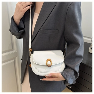 Detail of white matte leather saddle bag featuring a gold horseshoe metal buckle
