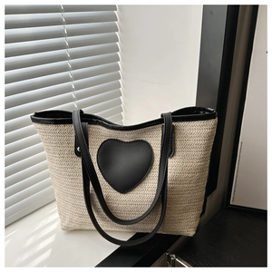 Detail of woven straw tote bag featuring black heart patch and leather handles