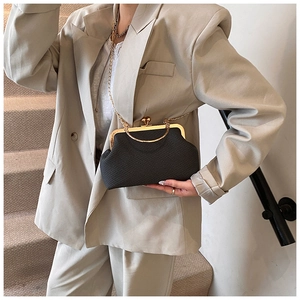Détail d'un sac bandoulière tissé noir avec monture dorée et chaîne sur blazer beige