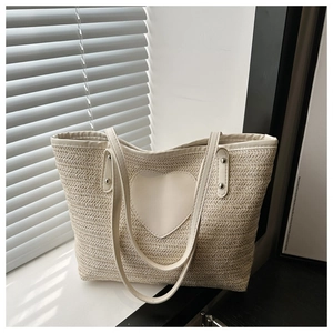 Detail of beige woven tote bag featuring a heart leather patch and dual shoulder straps