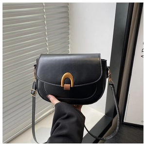 Detail of a black leather saddle bag featuring a gold U-shaped buckle and adjustable strap
