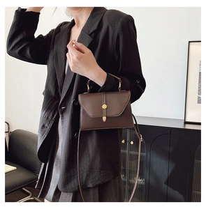 Detalle del bolso bandolera de cuero PU marrón oscuro con hebilla dorada sobre un blazer
