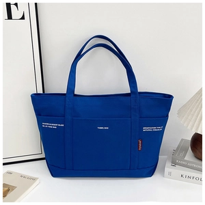 Detailed close-up of blue canvas tote bag with front pocket and white logo on white desk