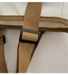 Detail view of the adjustable black plastic buckle on a beige canvas shoulder bag strap