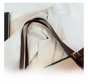 Detail of adjustable burgundy leather straps with gold buckles on a beige tote bag