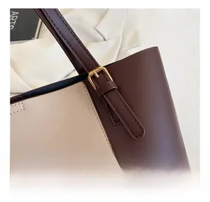 Close-up of golden metal buckle and brand logo on a two-tone leather tote bag