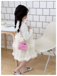 Pink kids crossbody bag with large bow and chain strap worn by girl in lace dress