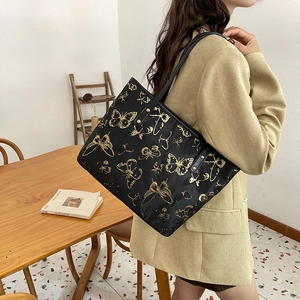 Detail of black tote bag with gold butterfly print worn over the shoulder by model