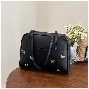 Détail du cabas noir mat avec six ornements papillon en métal argenté sur un bureau