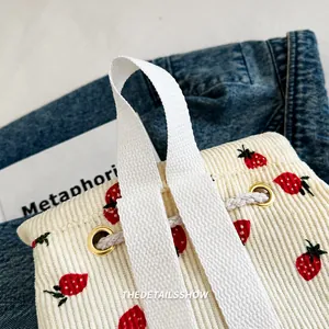 Detail of white corduroy tote bag featuring red strawberry prints and durable handles