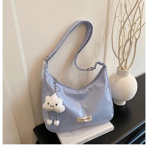 Detail van lichtblauwe nylon hobo tas met wolkenhanger op een witte boek achtergrond