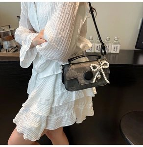 Detail of grey crossbody bag with vintage texture, pearl bow, and heart charm