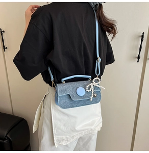 Detail view of the light blue denim crossbody bag with a pearl bow and metal heart charm