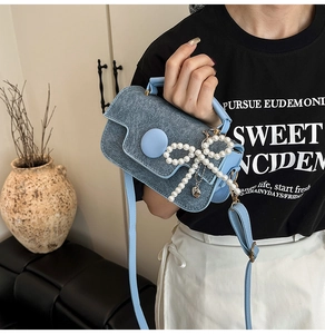 Detail of light blue denim mini bag with large pearl bow and elegant gold hardware
