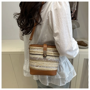 Detail of woven straw bucket bag featuring brown leather straps and gold metal buckle