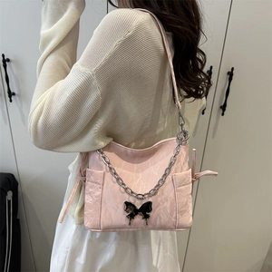 Sac bandoulière rose avec boucle papillon et chaîne argentée porté sous le bras