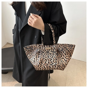 Detail of leopard print tote bag with gold metal plaque shown on model in black coat