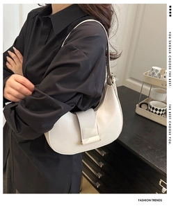 Close-up of minimalist creamy white crescent shoulder bag shown in an indoor setting