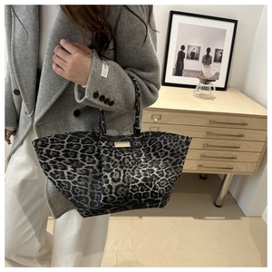 Detailed shot of leopard print tote bag featuring a gold metal brand plate and sturdy handles