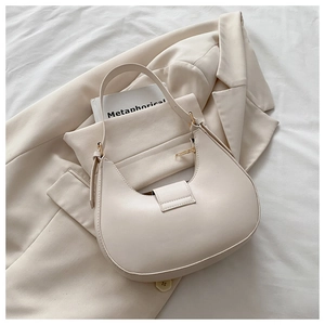 Detail of off-white crescent shoulder bag with gold hardware on a beige blazer