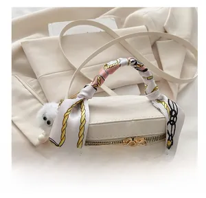 Detail showing white barrel handbag with silk scarf handle and plush pompom charm