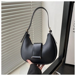 Detail of matte black crescent bag with golden metal trim and adjustable strap