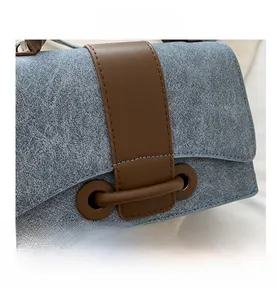 Detail view of light blue denim fabric texture and brown leather trim on the handbag