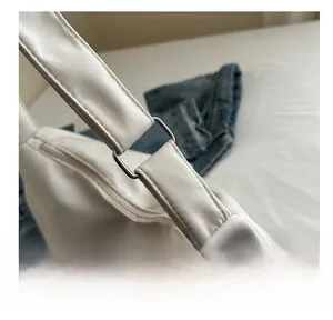 Detail of silver metal D-ring buckle and sturdy stitching on white nylon crossbody bag