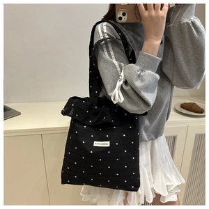 Détail d'un sac cabas en toile noire avec motif floral, volants et étiquette blanche